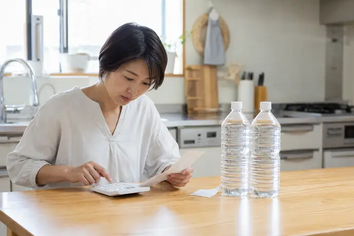 ペットボトルのレシートと電卓を使って1Lあたりの実質単価を計算する女性