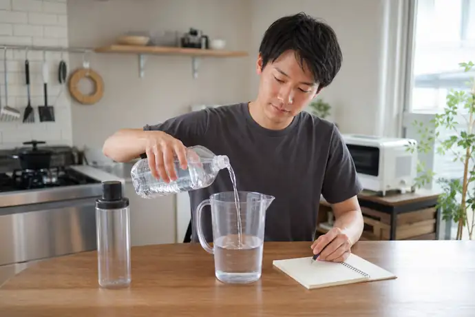 一人暮らしのキッチンで水を計量しながら使用量を記録する男性