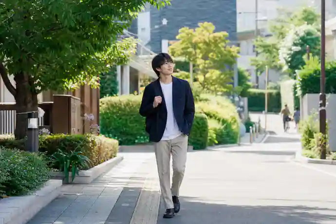緑の多い日本の街並みを前向きに歩く若い社会人の様子