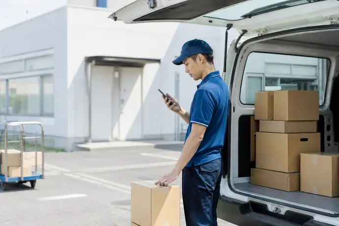 配送ステーションで荷物を積み込み、スマートフォンでルートを確認する配達員の場面