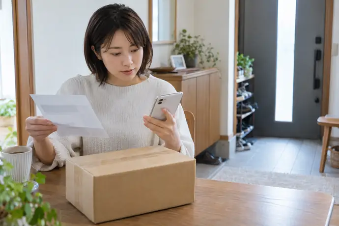 配達通知とスマートフォンを見比べ、荷物の受取場所を確認する人。