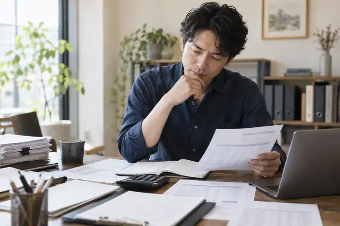契約書と精算明細、入金記録を並べてファクタリングの仕訳を確認する個人事業主の様子