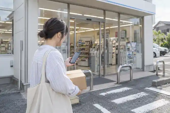 コンビニへ出かける前にスマートフォンで発送受付設備を確認する場面