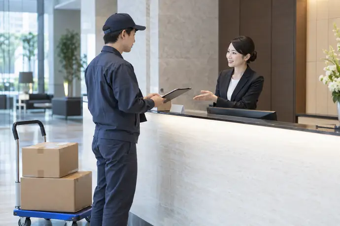 オフィスビルの受付で納品先と受領方法を確認する軽貨物ドライバーの仕事風景