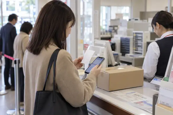 郵便局の窓口で受領証を受け取り、スマートフォンで追跡番号を確認する場面