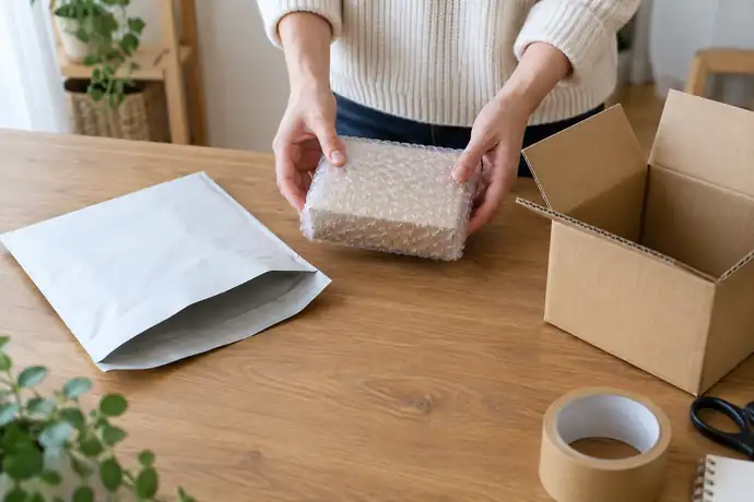 厚みのある小型荷物と未使用の発送資材を机に並べ、発送手段を比べている様子
