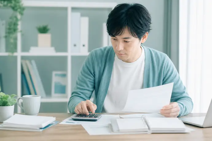 個人事業主が電卓と帳簿を使いインボイスの申告方式ごとの税額を比較している自然な仕事風景