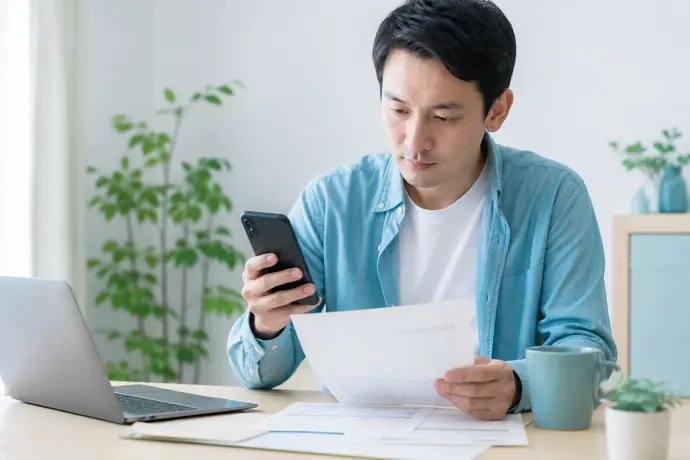 自宅で仕事用スマートフォンの利用状況を確認し通信費の按分を整理する個人事業主の自然な仕事風景