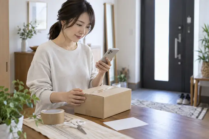 発送する荷物を用意し、営業所の情報をスマートフォンで確認する人の様子