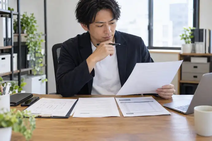 事業者がイベント設営の契約書、発注書、請求明細を机に並べ、支払条件と債権譲渡条項を照合している様子