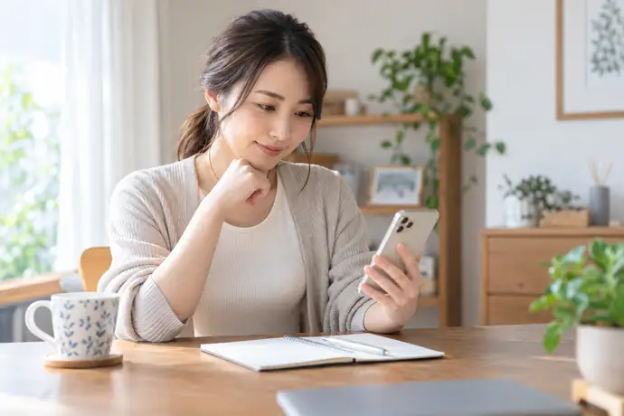 自宅の机でスマートフォンを使い整形外科の受付情報を確認する人